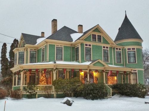 A charming green Victorian house adorned with holiday decorations, surrounded by snow on a winter day.