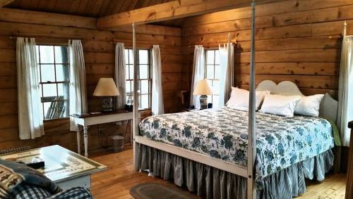 Cozy wooden bedroom with a four-poster bed, floral bedding, and natural light from windows.