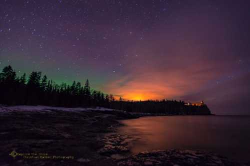 A serene night scene with a starry sky, glowing horizon, and rocky shoreline surrounded by trees.