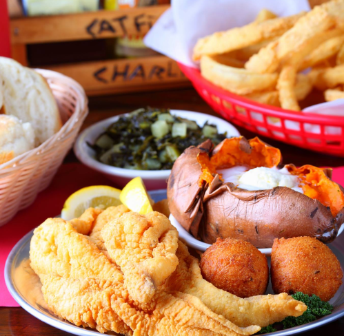 A plate of fried catfish, cornbread, sweet potato, collard greens, and fries, garnished with lemon slices.