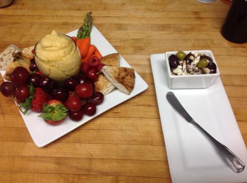 A platter of assorted fruits, hummus, pita, and vegetables, alongside a small dish of olives and feta cheese.