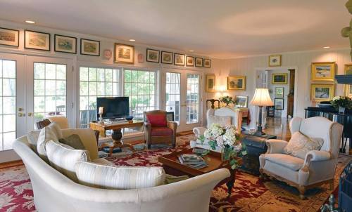 Cozy living room with large windows, comfortable seating, a TV, and framed artwork on the walls. Bright and inviting atmosphere.