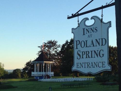 Sign for "Inns at Poland Spring Entrance" with a gazebo and chairs set up in the background under a clear sky.