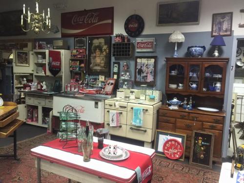 A vintage shop display featuring Coca-Cola memorabilia, antique furniture, and decorative items on a patterned rug.