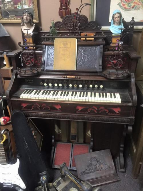An antique organ with ornate details, surrounded by vintage decor and musical instruments in a cozy setting.