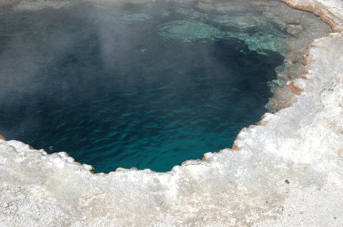 A close-up of a geothermal hot spring with clear blue water and steam rising from the surface.