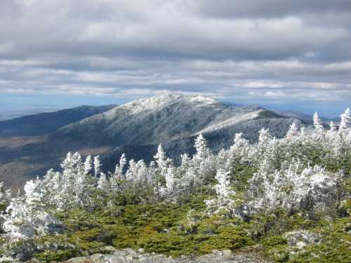 Snow-covered mountain peak with frosted trees in the foreground under a cloudy sky.