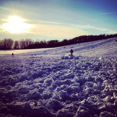 A snowy landscape with people enjoying the outdoors under a bright sun and clear blue sky.