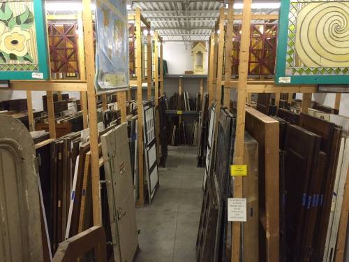 A storage area filled with various wooden doors and stained glass panels, organized on shelves.