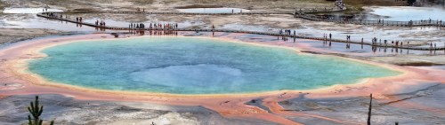 A vibrant geothermal pool with blue water and colorful mineral deposits, surrounded by visitors and natural scenery.