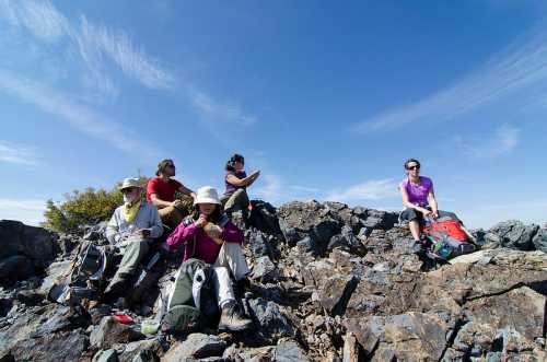 A group of hikers resting on rocky terrain under a clear blue sky, enjoying the outdoors together.