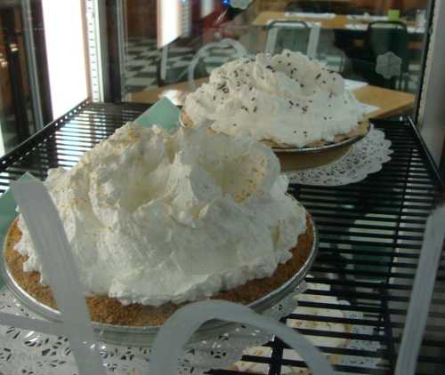 Two pies topped with fluffy whipped cream, displayed on a rack with a lace doily underneath.