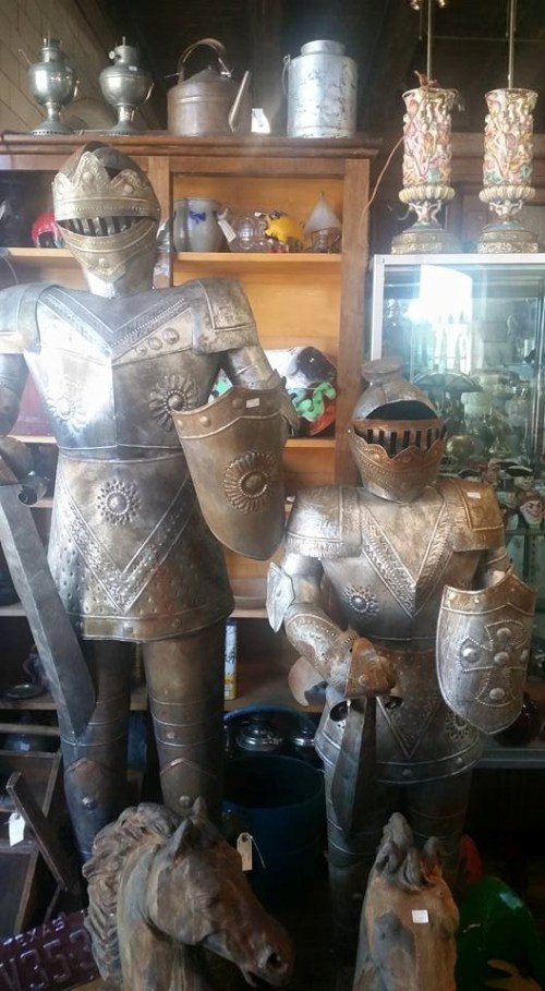 Two decorative knight statues in armor, one larger than the other, displayed among various antiques in a shop.