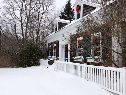 A snowy scene of a house decorated for the holidays, featuring wreaths and red bows on the windows.