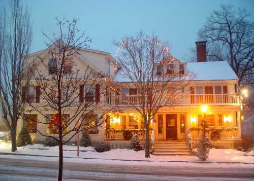 A charming, snow-covered inn adorned with holiday lights and decorations, glowing warmly in the evening.