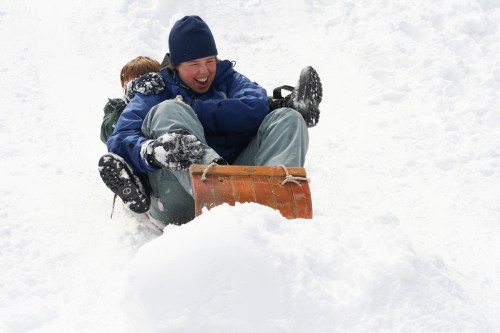Two people joyfully sledding down a snowy hill, laughing and enjoying the winter day.