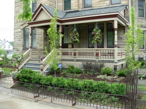 A charming stone house with a porch, hanging flower baskets, and a well-maintained garden surrounded by a decorative fence.