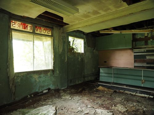 Abandoned room with peeling paint, broken windows, and debris on the floor, featuring a faded sign that reads "SOTY ENTR."
