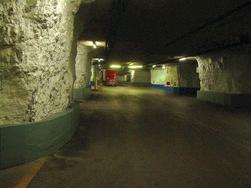 Dimly lit underground tunnel with rough stone walls and a red truck parked in the distance.