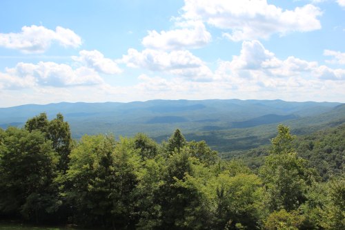 A panoramic view of rolling green mountains under a bright blue sky with fluffy white clouds.