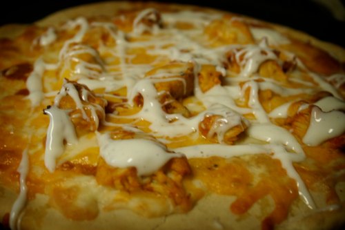 Close-up of a pizza topped with chicken, melted cheese, and drizzled with white sauce.
