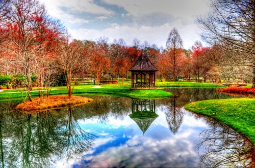 A serene park scene featuring a gazebo by a pond, surrounded by colorful trees and a reflective water surface.