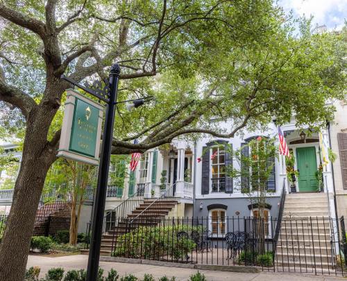 Historic building with green doors, American flags, and a sign under a large tree in a charming neighborhood.