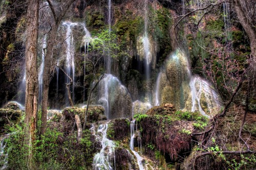 A serene waterfall cascading over moss-covered rocks, surrounded by lush greenery and trees.