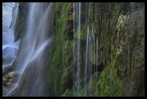A serene waterfall cascading over moss-covered rocks, creating a misty atmosphere in a lush green setting.
