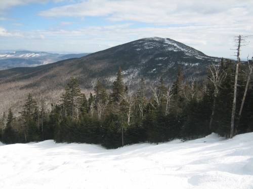 A snowy mountain landscape with a prominent peak in the background, surrounded by evergreen trees and a clear sky.