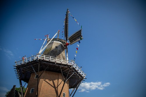 A tall windmill with colorful flags against a clear blue sky, showcasing its wooden structure and rotating blades.