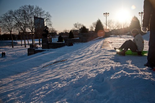 A snowy hill at sunset with people sledding and enjoying winter activities.