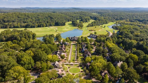 Aerial view of a lush green landscape featuring a golf course, a lake, and a cluster of homes surrounded by trees.
