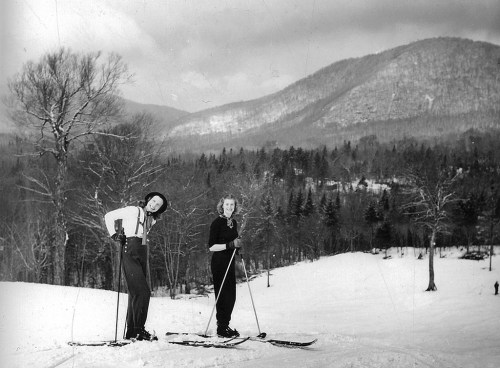 Two skiers pose on a snowy slope with mountains in the background, enjoying a winter day outdoors.