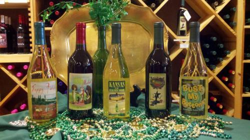 A display of six wine bottles with colorful labels, surrounded by green beads and a gold tray in a wine shop.