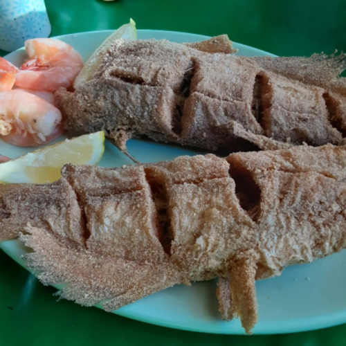 A plate of fried fish with sliced lemon and shrimp on the side, served on a green table.