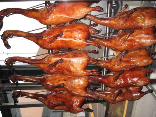A row of roasted ducks hanging on a rack, glistening with a golden-brown glaze.