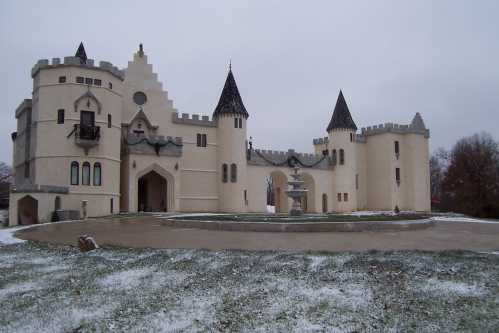 A snow-covered castle with turrets and a fountain in front, set against a gray sky.