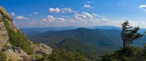 A panoramic view of rolling green mountains under a blue sky with scattered clouds.