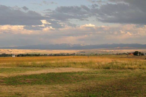A scenic landscape featuring grassy fields, distant mountains, and a cloudy sky.