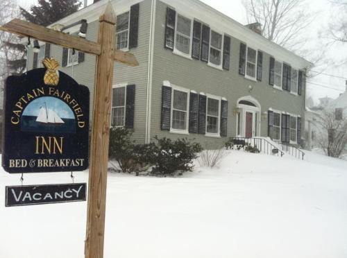 A snow-covered bed and breakfast with a "Vacancy" sign in front, surrounded by a winter landscape.