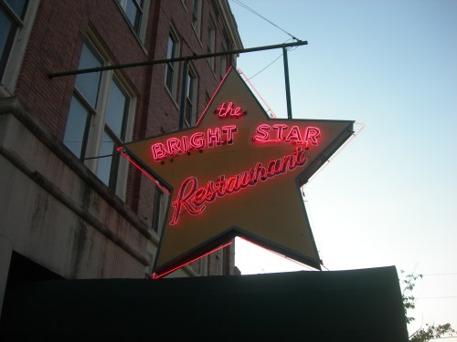 Neon sign of "The Bright Star Restaurant" in the shape of a star, hanging above a building at dusk.