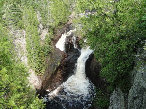 A cascading waterfall flows through rocky terrain, surrounded by lush green trees and foliage.