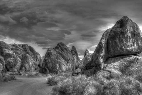 A dramatic black and white landscape featuring large rock formations and a cloudy sky.