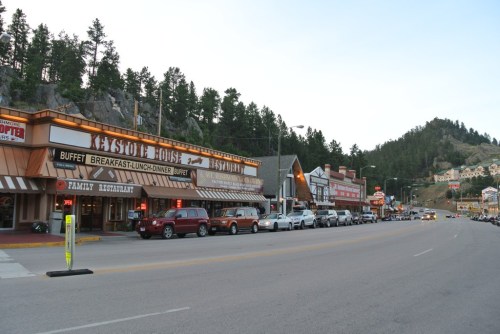 A street view of Keystone, South Dakota, featuring restaurants and shops with mountains in the background.