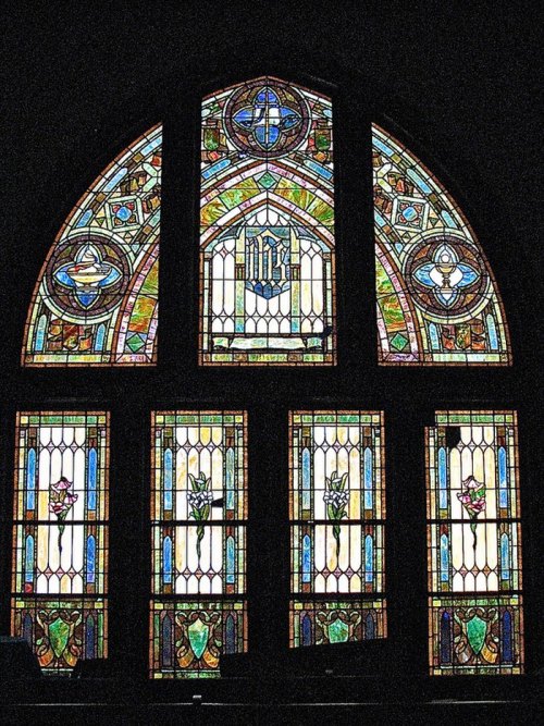 Colorful stained glass windows featuring intricate designs and floral motifs, illuminated against a dark background.
