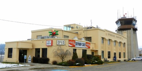 Historic Spokane Airport building with a control tower, featuring a café and a bright "Open" sign. Snow on the ground.