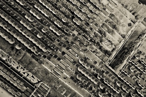 Aerial view of an abandoned area with rows of empty chairs and graffiti on the ground, presented in black and white.