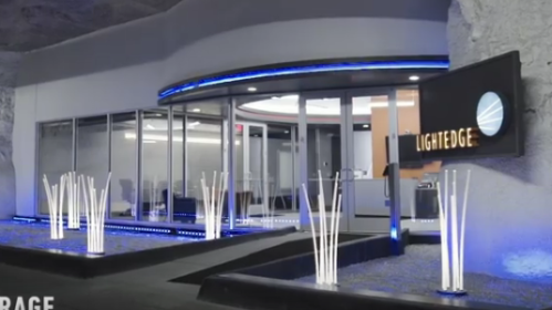Modern entrance of a facility with sleek design, illuminated features, and decorative white plants.