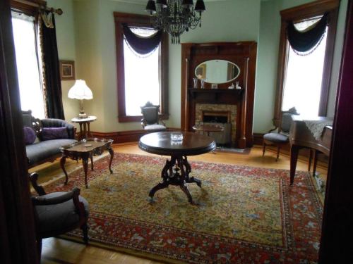 A vintage living room with elegant furniture, a chandelier, and a decorative rug, featuring a fireplace and large windows.
